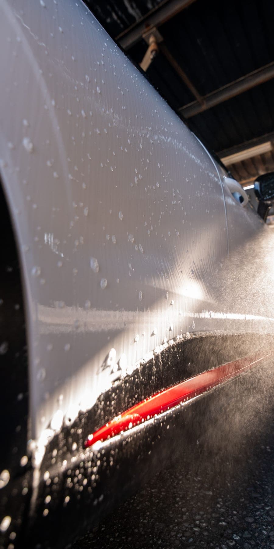 Lateral de un coche blanco con reflejos del sol y gotas de agua
